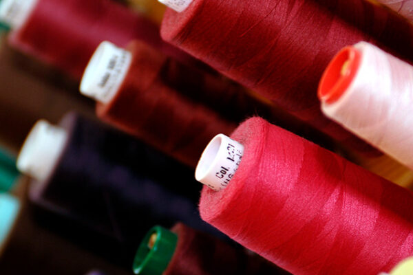 Spools of vibrant colored thread, including shades of red, pink, and green, are neatly arranged in rows, showcasing a rich spectrum of hues. The focus is on the smooth texture and orderly placement, suggesting a sewing or crafting context.